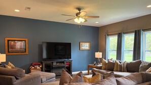A living room with a flat-screen TV, a ceiling fan, and a large window with curtains. - Delightful 4-bedroom house with AC in charming High Point (High Point)