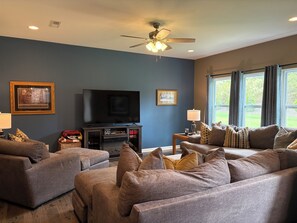 A living room with a flat-screen TV, a ceiling fan, and a large window with curtains. - Delightful 4-bedroom house with AC in charming High Point (High Point)