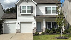 A two-story house with a garage, a front porch, and a small tree in the front yard. - Delightful 4-bedroom house with AC in charming High Point (High Point)