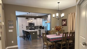 A modern kitchen with white cabinets, a central island, and a dining area with a plaid tablecloth. - Delightful 4-bedroom house with AC in charming High Point (High Point)