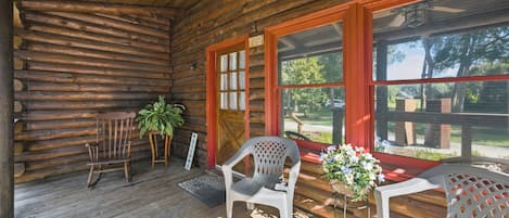 A log cabin with a porch, wooden benches, a welcome sign, and a potted plant.