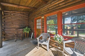 A log cabin with a porch, wooden benches, a welcome sign, and a potted plant.