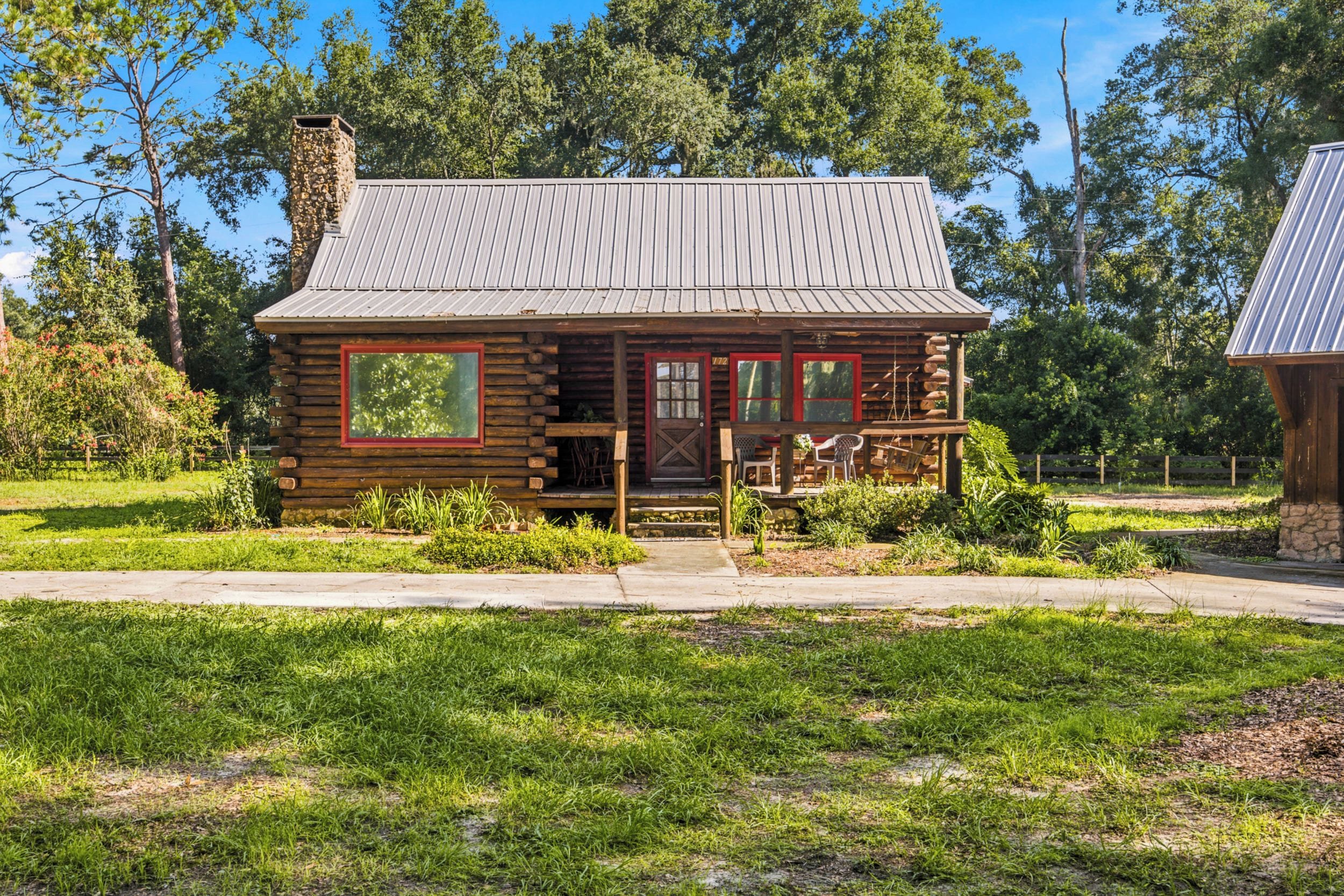 A rustic log cabin with a metal roof, a chimney, and a porch with outdoor seating.