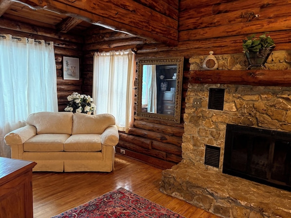 L’intérieur d’une cabane en rondins, avec un canapé, une cheminée, un miroir et un mur en pierre.