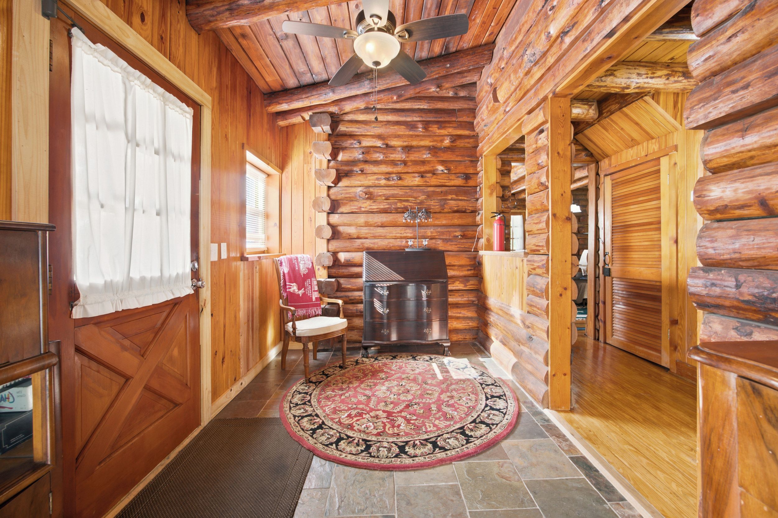 A log cabin interior with a fireplace, a ceiling fan, and a rug.