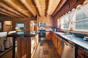 A log cabin interior with a kitchen area featuring wooden cabinets, a stove, and a sink.