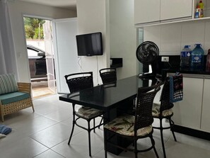 A dining area with a black table and chairs, a TV mounted on the wall, and a fan. - Beachfront house - Bertioga (Bertioga)