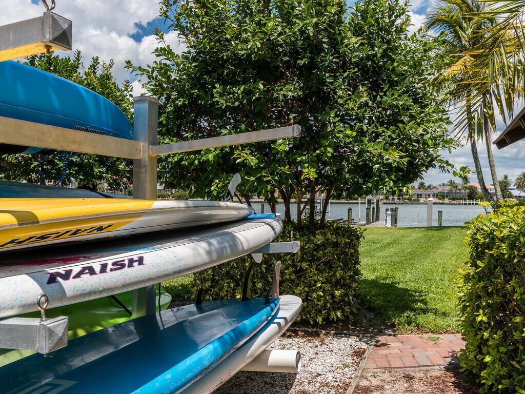 A row of kayaks with the brand "NAISH" on a dock by a body of water, surrounded by greenery.