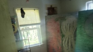 A room with a window, a wall with a colorful mural, a wooden floor, and a small table. - Spacious 4-bedroom estate in adorable Carmel Hamlet with AC (Carmel Hamlet)