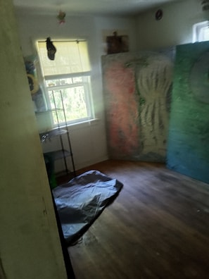 A room with a window, a wall with a colorful mural, a wooden floor, and a small table.