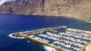 Ein Yachthafen mit vor Anker liegenden Booten, eine Pier, die sich ins Wasser erstreckt, und eine felsige Klippe im Hintergrund.