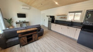 A modern kitchen with a built-in oven, a dining area with a wooden table and sofa, and a TV mounted on the wall.