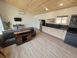 A modern kitchen with a built-in oven, a dining area with a wooden table and sofa, and a TV mounted on the wall.