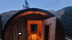 A wooden sauna with a bench and a bench seat, a door, and a view of the surrounding landscape.