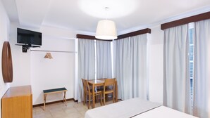 Une chambre d’hôtel comprenant un lit, un bureau avec une chaise, un téléviseur fixé au mur et une fenêtre avec des rideaux.