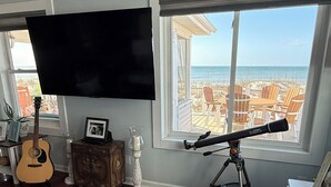 Un soggiorno con una grande TV, una chitarra, un telescopio e vista sulla spiaggia.