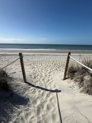 A sandy beach with wooden posts and a rope barrier. - Amazing 3-bedroom beach house with an enchanting view, screen porch & deck (Oak Island)