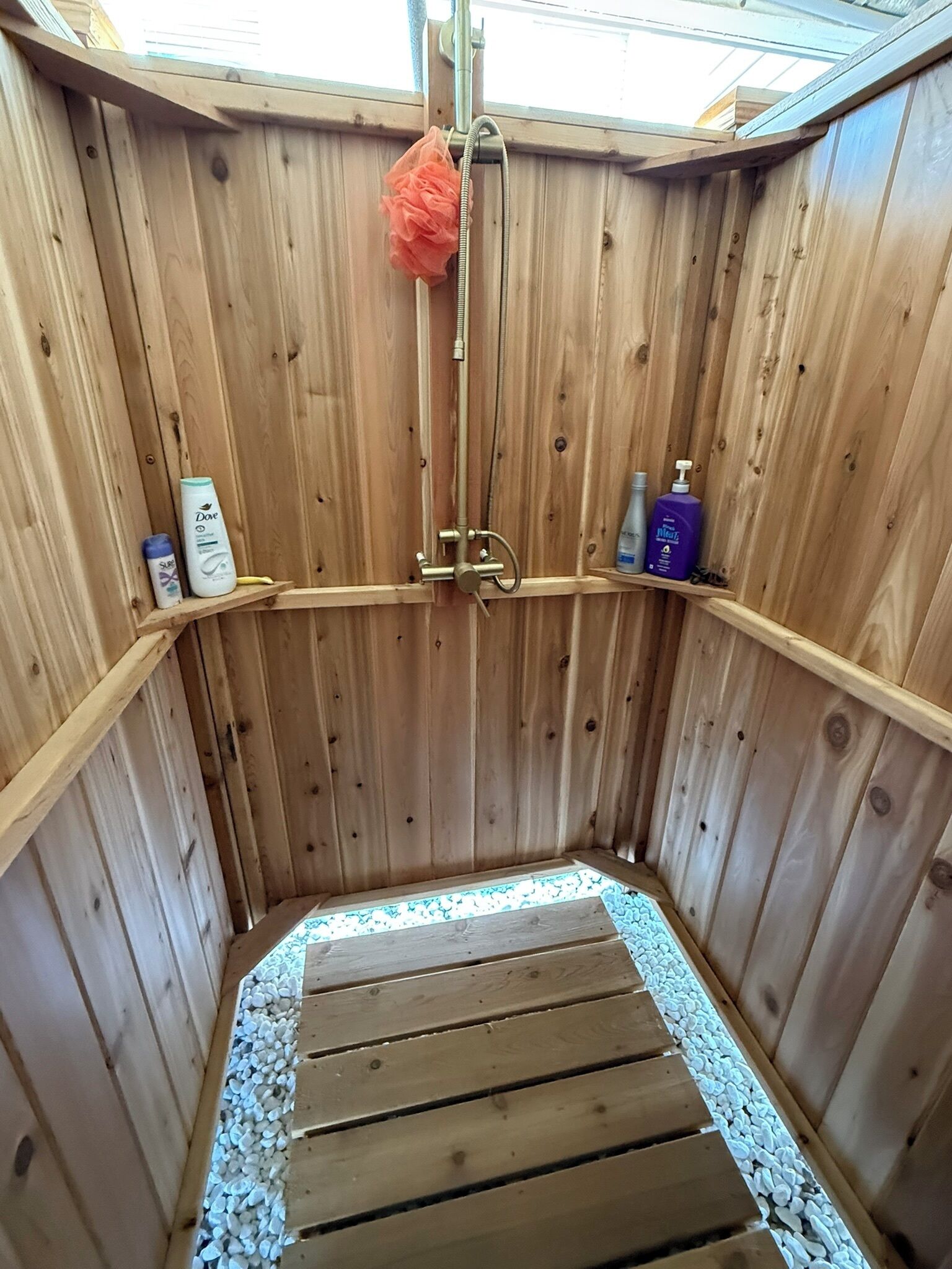 A wooden sauna with a bench, a shower head, and shelves with personal care items.
