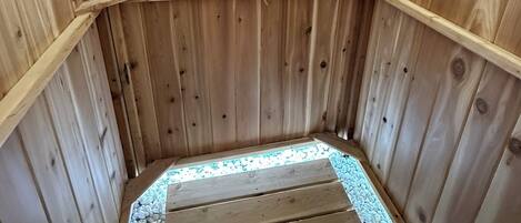 A wooden sauna with a bench, a shower head, and shelves with personal care items.