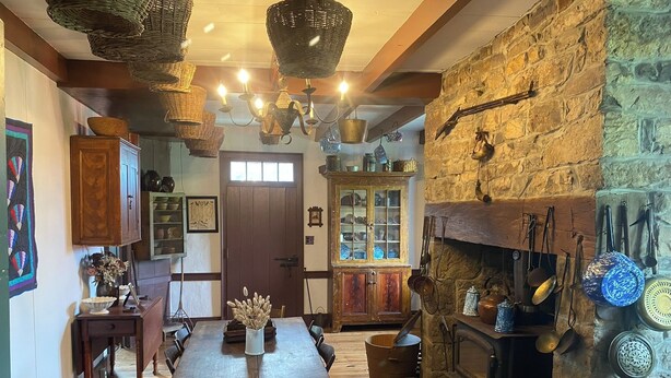 A rustic kitchen with a wooden table, chairs, a stone wall, and a fireplace.