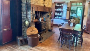 A rustic interior with a stone fireplace, wooden dining table, and vintage kitchenware.