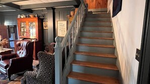 A staircase with wooden steps and a white railing, leading to a room with a dark wooden floor and a cushioned chair.