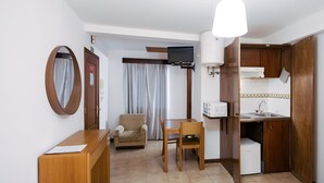 Ein kompaktes Hotelzimmer mit Küchenzeile, einem Essbereich mit Tisch und Stühlen, einer Couch und einem großen Spiegel.