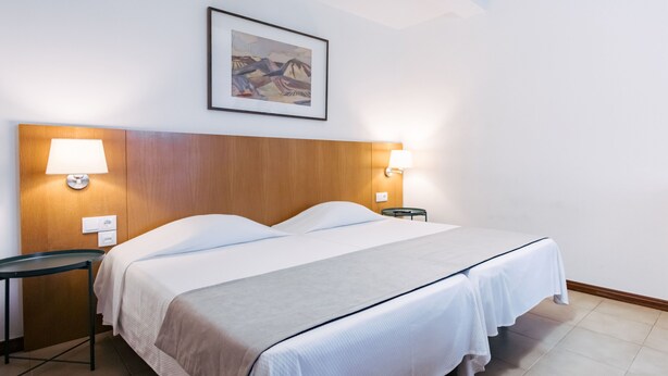 Ein Hotelzimmer mit einem Doppelbett, zwei Nachttischen, einem Wandbild und zwei Wandlampen.