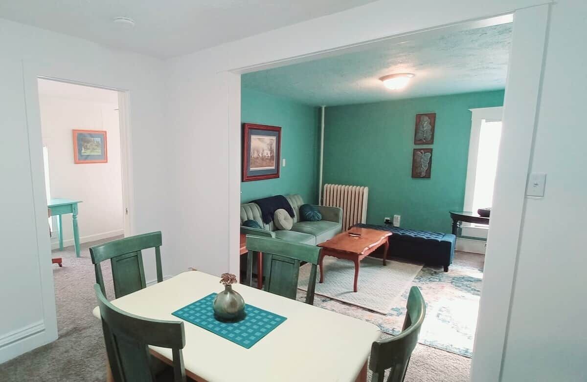 Et spiseområde med bord og stole, en sofa og en radiator i et rum med teal vægge.