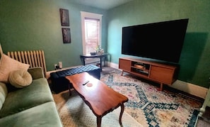 A living room with a sofa, a coffee table, a TV, and a patterned rug. - Earthvine: Cozy Zen Retreat Pets-OK Downtown-ISU (Ames)
