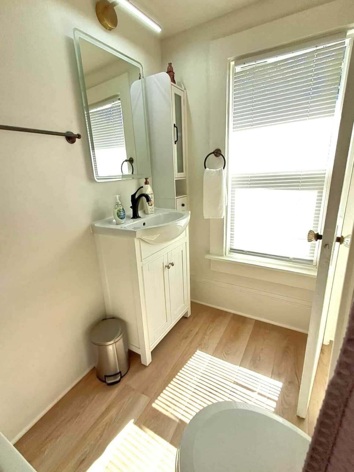 Ein Badezimmer mit Toilette, Waschbecken, Spiegel und Fensterjalousien.