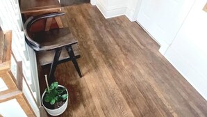 A hallway with a wooden floor, a small table with a plant, a chair, and a door with a number. - Windrose: Tranquil Pets-OK Soak Tub Suite Near ISU (Ames)