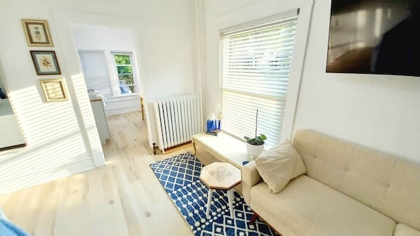 Un salon avec un canapé, une petite table, un radiateur et une fenêtre avec des stores.