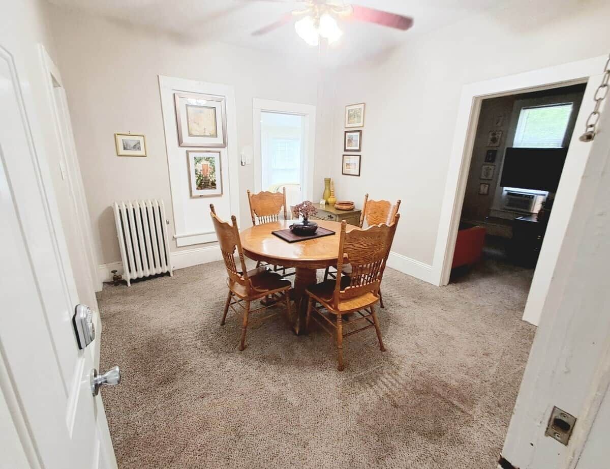 A dining area with a round table and chairs, a ceiling fan, and a radiator.