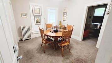 A dining area with a round table and chairs, a ceiling fan, and a radiator.