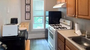 Eine Küche mit Gasherd, Backofen, Spüle und Holzschränken. Ein Fenster mit Jalousien, ein Toaster und ein Kühlschrank sind ebenfalls vorhanden.