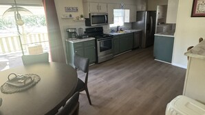 A compact kitchen with a dining area, including a table with chairs, a microwave, stove, refrigerator, and a small window.