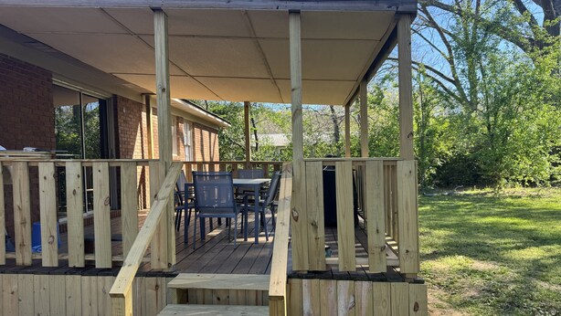 A wooden deck with a covered seating area, a staircase, and a view of a brick building.