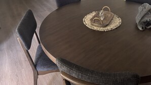 A dining area with a round table, chairs, a clear pendant light, and a kitchen in the background.