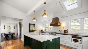 Una cocina con una isla grande, suelo de madera, luces colgantes, estufa y microondas.