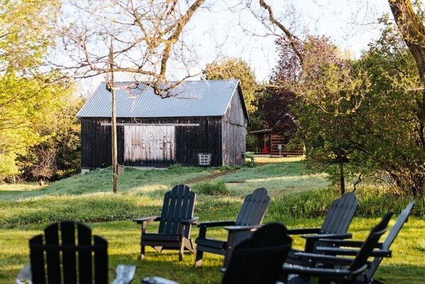 A rustic barn with a metal roof, surrounded by a grassy area with Adirondack chairs.