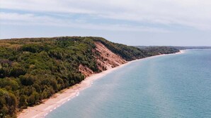 Un paisaje costero con una playa, colinas boscosas y cielo despejado.