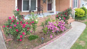 A brick house with a porch, two windows, a star decoration, and a garden with pink flowers. - Beautiful 4BR/3BA Fully Furnished Home in Quiet Neighborhood (Evans)