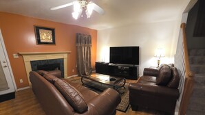 A living room with leather sofas, a fireplace, a flat-screen TV, and a staircase. - Beautiful 4BR/3BA Fully Furnished Home in Quiet Neighborhood (Evans)