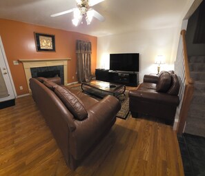A living room with leather sofas, a fireplace, a flat-screen TV, and a staircase. - Beautiful 4BR/3BA Fully Furnished Home in Quiet Neighborhood (Evans)