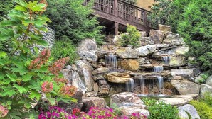Un jardin avec une cascade, des rochers et des fleurs roses.