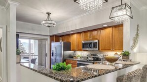 Une cuisine moderne dotée de plans de travail en granit, d’appareils électroménagers en acier inoxydable, d’armoires en bois et d’un grand îlot central.
