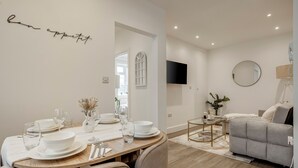 Un coin repas avec une table dressée pour quatre personnes, un canapé, un téléviseur et un miroir au mur.