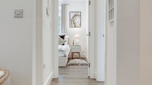 Un couloir mène à une chambre à coucher qui contient un lit, une table de chevet et un tableau encadré accroché au mur.