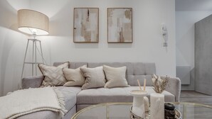 Un salon moderne avec un canapé gris, une table basse en verre, un lampadaire et des œuvres d’art abstraites accrochées au mur.